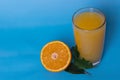 Fresh orange juice in a glass with fruit cut in half and sliced by green leaves isolated on a blue background, top view Royalty Free Stock Photo