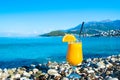 Fresh orange juice in a glass with a straw and an orange slice on a pebble beach against the backdrop of a clear calm sea Royalty Free Stock Photo