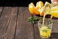 Fresh orange juice is poured into a glass with ice and mint leaves. On the table are orange slices and mint leaves. Dark wooden