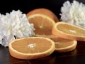 Fresh orange slices and a half orange laying on a black tile counter with two white carnations for decoration.  Fresh citrus fruit Royalty Free Stock Photo