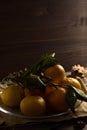 Fresh orange tangerines with green leaves in a glass plate on a wooden background. ripe fruits on a dark table. low key. vertical Royalty Free Stock Photo