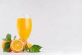 Fresh oranges juice in wineglass with ripe half oranges and green leaf on soft white wood table, copy space. Royalty Free Stock Photo