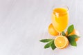 Fresh oranges juice in wineglass with ripe half oranges and green leaf on soft white wood table, top view, copy space. Royalty Free Stock Photo