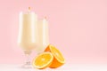 Fresh oranges milkshake in graceful glass with pieces juicy citrus, striped straws on pink background.