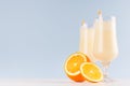 Fresh oranges milkshake with juicy pieces citrus and striped straw in gentle graceful soft light blue interior, copy space.