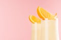 Fresh oranges milkshake with pieces juicy citrus, striped straws detail, closeup, top section on pink background.