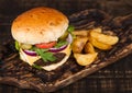 Fresh organic beef burger with cheese  and sauce with vegetables and potato vedges on wooden chopping board Royalty Free Stock Photo