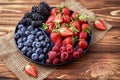 Fresh organic blueberries, blackberries, strawberries, raspberries on a separate dish on a textured wooden background