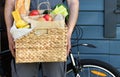 Fresh organic food in a wicker basket in the hands of a bicycle courier. Bike delivery or donation of food concept Royalty Free Stock Photo