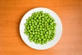 Fresh organic green peas in a white round bowl on a wooden table in soft focus, top view or flat lay of healthy raw vegan food Royalty Free Stock Photo