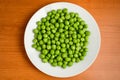 Fresh organic green peas in a white round bowl on a wooden table in soft focus, top view or flat lay of healthy vegan food Royalty Free Stock Photo