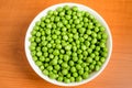 Fresh organic green peas in a white round bowl on a wooden table in soft focus, top view Royalty Free Stock Photo