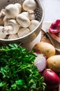 Fresh organic ingredients for preparing healthy vegetarian meal mushrooms in colander, potatoes, onion, parsley Royalty Free Stock Photo
