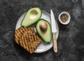 Fresh organic ripe avocado and whole grain grilled bread - delicious healthy breakfast, snack on dark background, top view