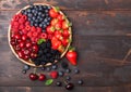 Fresh organic summer berries mix in round wooden tray on dark wooden table background. Raspberries, strawberries, blueberries, Royalty Free Stock Photo