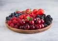 Fresh organic summer berries mix in round wooden tray on light kitchen table background. Raspberries, strawberries, blueberries, Royalty Free Stock Photo