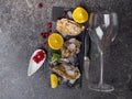 Fresh oysters in ice with lemon, cranberries, glass for wine or champagne, knife over stone table