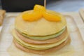 Fresh pancakes many color stacked layered with orange on wooden plate