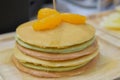 Fresh pancakes many color stacked layered with orange on wooden plate