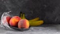 Fresh peaches in a plastic container with cling film and with bananas on a dark background Royalty Free Stock Photo