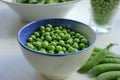 Fresh peeled green sugar snap peas in a bowl and open pods on a white wooden table background with copy space. Royalty Free Stock Photo