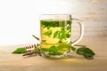 Fresh peppermint leaves brewed as a healthy herbal tea in a glass cup, some flowering stems on a light wood table, copy space, Royalty Free Stock Photo