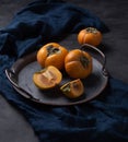 Fresh persimmon lies on a dish with a blue napkin on a wooden table