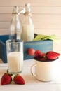Fresh picked strawberrys with glass of the milk on white wooden background.