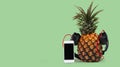 fresh pineapple with black headphones and smartphone with  black screen against green background Royalty Free Stock Photo