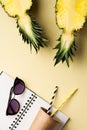 Fresh pineapple cut in two part, notebook or sketchbook and sunglasses on yellow background. Summer concept. Royalty Free Stock Photo