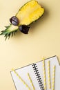 Fresh pineapple cut in two part, notebook or sketchbook and sunglasses on yellow background. Summer concept. Royalty Free Stock Photo