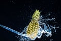 Fresh pineapple gets splashed with water on black background. Concept of summer, health and fun