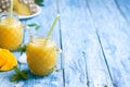 Fresh pineapple and mango smoothie in two glasses with fruits on a blue wooden rustic background with copy space on the Royalty Free Stock Photo