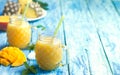 Fresh pineapple and mango smoothie in two glasses with fruits on a torquise wooden rustic background Royalty Free Stock Photo