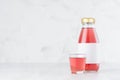 Fresh pink fruit juice in glass bottle with blank label mock up with glass on wood table in white interior, template for packaging