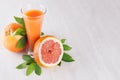 Fresh pink juice and grapefruits with green leaves on white wood board, copy space. Royalty Free Stock Photo