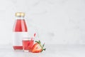 Fresh pink strawberry juice in glass bottle with blank label mock up with glass, straw, fruit slices in soft light white interior