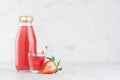 Fresh pink strawberry juice in glass bottle mock up with glass, straw, fruit slices in soft light white interior on wood table.