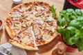 Fresh pizza with ham, hot pepper and capers and black olives on wooden table in restaurant. Royalty Free Stock Photo