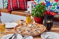 Fresh pizza with ham, hot pepper and capers and black olives on wooden table in restaurant. Royalty Free Stock Photo