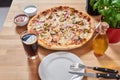 Fresh pizza with ham, hot pepper and capers and black olives on wooden table in restaurant. Royalty Free Stock Photo