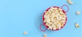 Fresh popcorn in a pink bowl on a blue background. Banner. Top view with copy space. The concept of snacks for cinemas