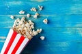 Fresh popcorn spilled from a cardboard striped cup on a blue wooden background with copy space