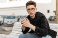 Fresh portrait serious young hipster man with vintage glasses in denim jacket with hairstyle on street at sunset. Attractive Royalty Free Stock Photo