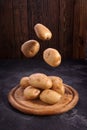 Fresh potatoes soaring above the wooden plate on wooden textured background. Organic food, carbs, tubers. Royalty Free Stock Photo