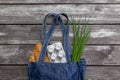 Fresh produce in blue denim market bag on wooden background, flat lay. Eco friendly reusable shopping bag for minimize waste,