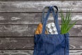 Fresh produce in blue denim market bag on wooden background, flat lay. Eco friendly reusable shopping bag for minimize waste,