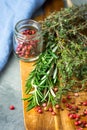 Fresh Provence Herbs Rosemary Thyme Twigs red Pink Peppers in Glass Jar on Aged Wood Cutting Board on Dark Concrete Stone Table