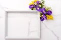 Fresh purple irises and yellow flowers bouquet, blank photo frame on white wooden background on white marble background. Spring, e Royalty Free Stock Photo