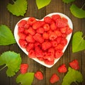 Fresh raspberries on a heart-shaped plate surrounded by green leaves on a wooden background Royalty Free Stock Photo